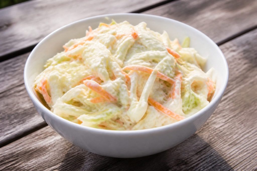 Bowl of creamy coleslaw with shredded cabbage and carrot in a mayo dressing, daylight picnic table