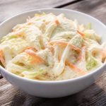 Bowl of creamy coleslaw with shredded cabbage and carrot in a mayo dressing, daylight picnic table