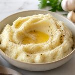 Bowl of creamy garlic mashed potatoes with melted butter and black pepper, daylight kitchen