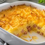 Baked hash brown breakfast casserole with golden potato top and melted cheddar in a white dish