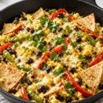 Cast iron breakfast burrito skillet with eggs, peppers, beans, cheese, and tortilla wedges