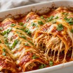 Baking dish of chicken enchiladas covered in red sauce and melted cheese