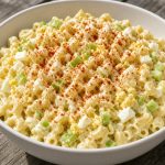 Bowl of classic macaroni salad with mayonnaise, celery, and paprika on a picnic table