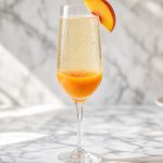 Peach bellini in a champagne flute with peach puree and a peach slice garnish