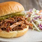 Pulled pork sandwich on a bun with pickle slices and slaw